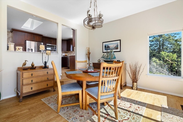 dining space with light wood-style floors, a skylight, baseboards, and a notable chandelier