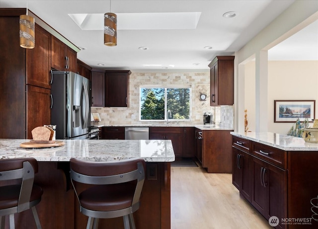 kitchen featuring a skylight, decorative backsplash, a kitchen bar, and appliances with stainless steel finishes
