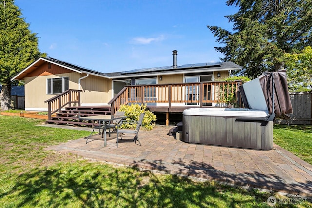 rear view of property featuring a patio area, a lawn, roof mounted solar panels, a hot tub, and a wooden deck