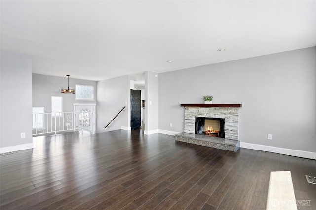 unfurnished living room featuring dark wood-type flooring, a stone fireplace, visible vents, and baseboards