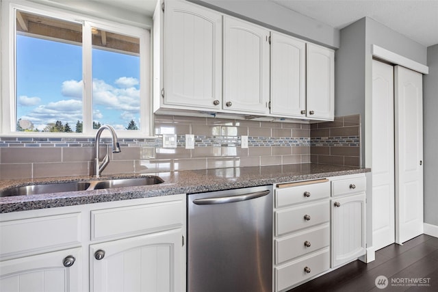 kitchen featuring stainless steel dishwasher, backsplash, a sink, and dark stone countertops
