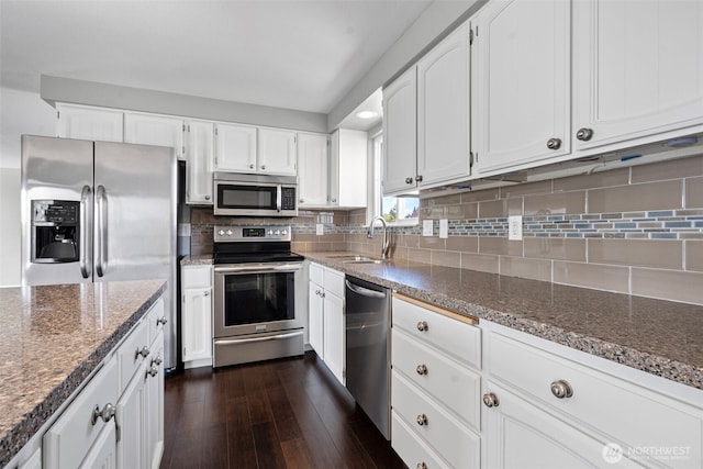 kitchen featuring white cabinets, stainless steel appliances, a sink, and dark stone counters