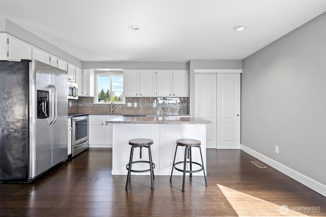 kitchen with white cabinets, stainless steel appliances, visible vents, and decorative backsplash