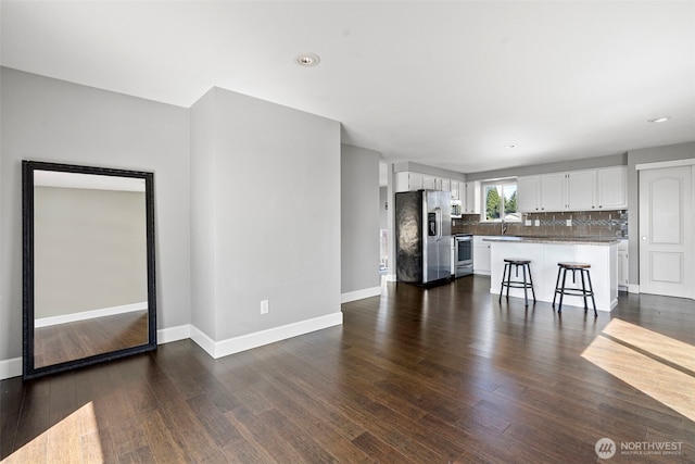 unfurnished living room featuring recessed lighting, baseboards, dark wood-type flooring, and a sink