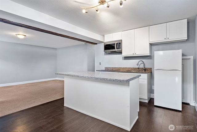 kitchen featuring white cabinetry, a sink, stainless steel microwave, freestanding refrigerator, and dark wood-style flooring