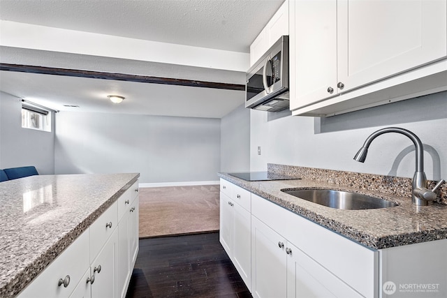 kitchen featuring dark wood finished floors, a sink, stainless steel microwave, light stone countertops, and white cabinetry