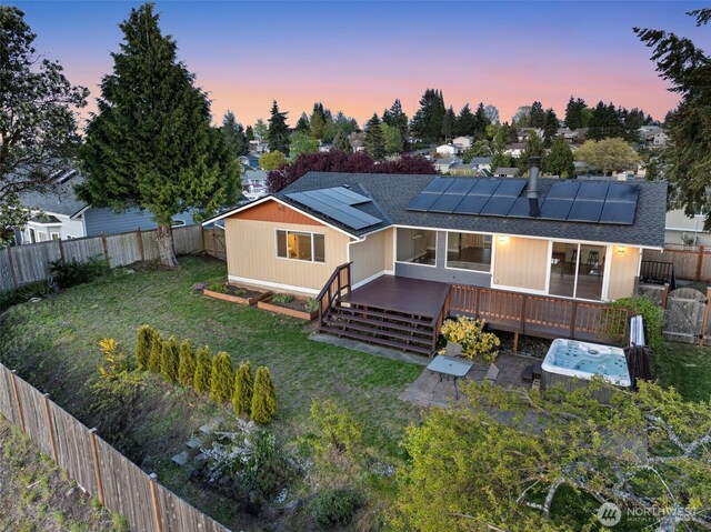 rear view of property with a fenced backyard, a wooden deck, roof mounted solar panels, and a yard