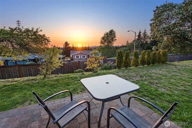 patio terrace at dusk with a fenced backyard and a yard