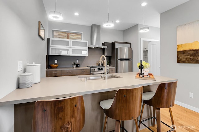kitchen with wall chimney range hood, stainless steel appliances, a sink, a kitchen breakfast bar, and pendant lighting