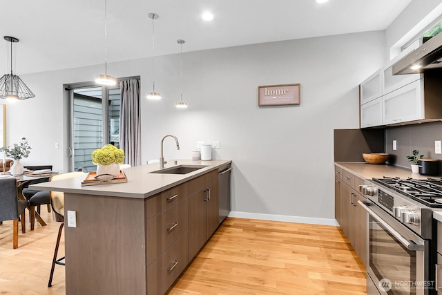 kitchen with a sink, stainless steel appliances, a peninsula, light wood finished floors, and light countertops