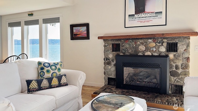 living area with a stone fireplace, visible vents, wood finished floors, baseboards, and a water view