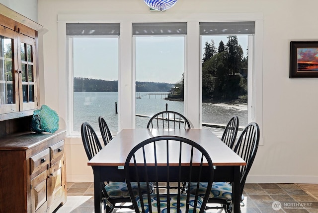 dining room featuring stone tile flooring, baseboards, and a water view