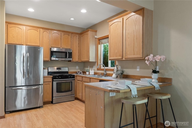 kitchen with light wood finished floors, light brown cabinets, a sink, a peninsula, and appliances with stainless steel finishes