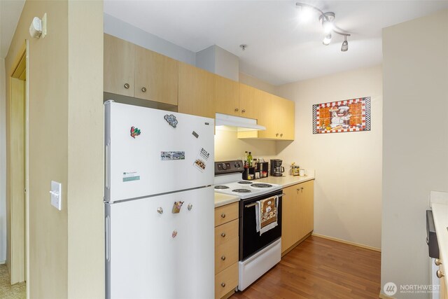 kitchen featuring light wood-type flooring, light countertops, light brown cabinets, under cabinet range hood, and white appliances