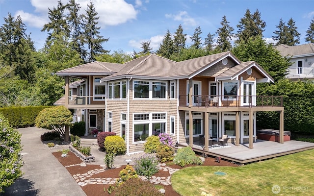 rear view of house with a hot tub, a balcony, a lawn, a wooden deck, and a tile roof