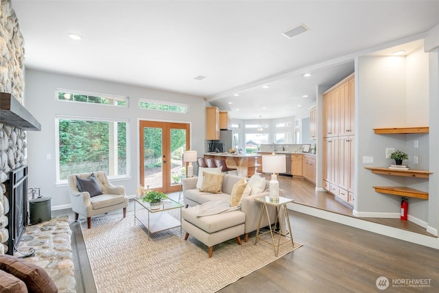 living room with wood finished floors, a stone fireplace, recessed lighting, baseboards, and french doors