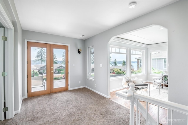 carpeted entryway featuring french doors, arched walkways, and baseboards