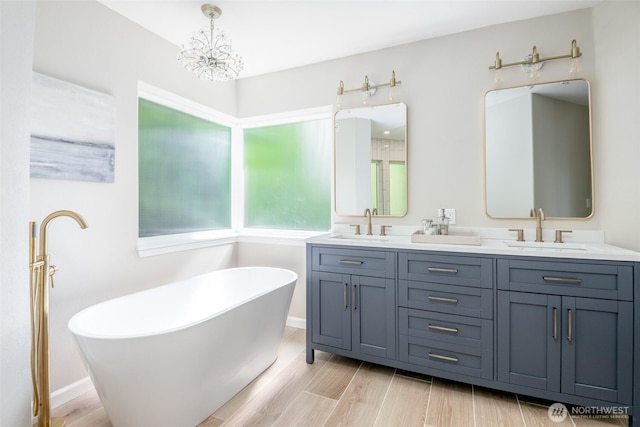 bathroom with a freestanding bath, double vanity, a chandelier, and wood finished floors