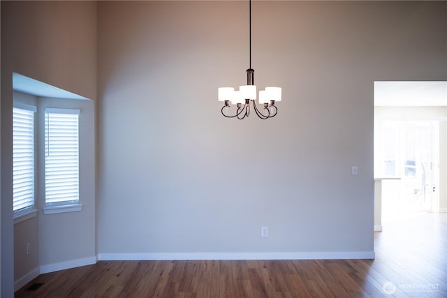 unfurnished dining area featuring baseboards, wood finished floors, and an inviting chandelier