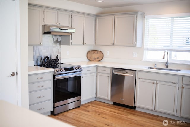 kitchen featuring a sink, appliances with stainless steel finishes, light countertops, under cabinet range hood, and light wood finished floors