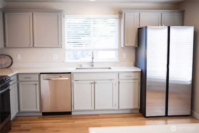 kitchen with stainless steel appliances, light countertops, light wood finished floors, a sink, and gray cabinetry