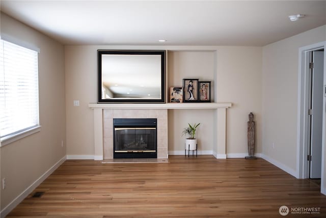 unfurnished living room featuring a tiled fireplace, visible vents, wood finished floors, and a healthy amount of sunlight