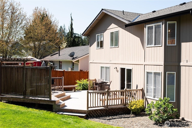 rear view of property featuring fence, roof with shingles, and a wooden deck
