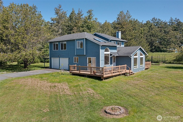back of house with an attached garage, a chimney, a deck, a shingled roof, and driveway