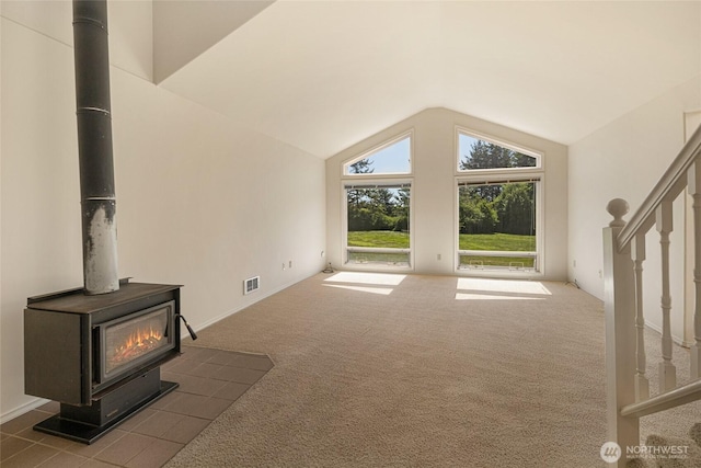 unfurnished living room with vaulted ceiling, a wood stove, carpet flooring, and stairway