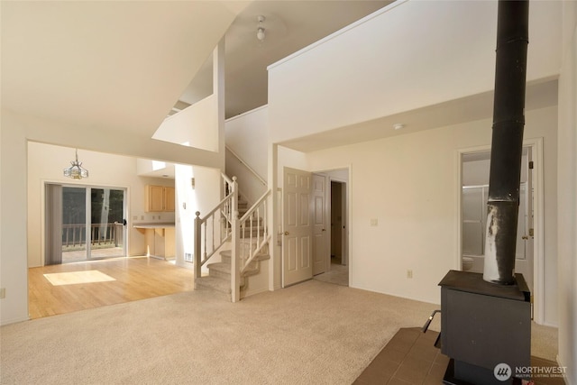 unfurnished living room with stairs, a wood stove, high vaulted ceiling, and carpet floors