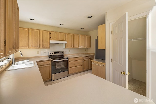 kitchen with a sink, under cabinet range hood, light brown cabinetry, light countertops, and stainless steel range with electric cooktop