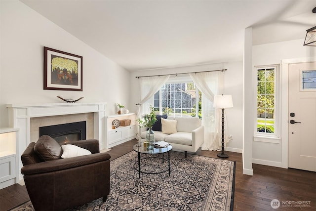 living area with a glass covered fireplace, baseboards, vaulted ceiling, and hardwood / wood-style flooring