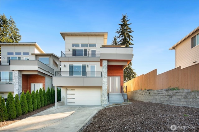 modern home with a garage, fence, a balcony, stucco siding, and driveway