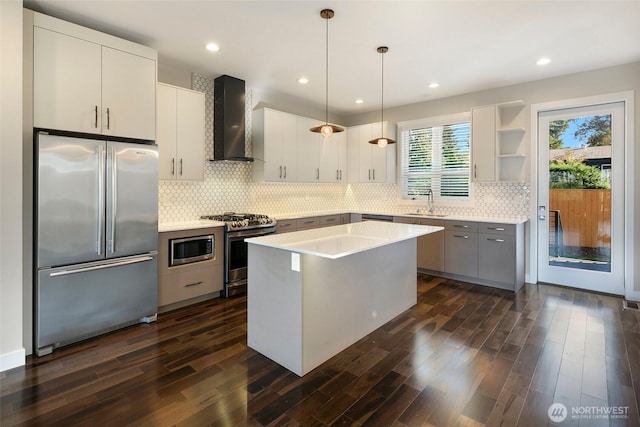 kitchen featuring dark wood-style flooring, appliances with stainless steel finishes, tasteful backsplash, a sink, and wall chimney exhaust hood