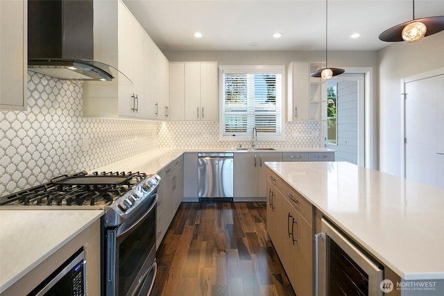 kitchen with wall chimney range hood, appliances with stainless steel finishes, a sink, dark wood-style floors, and beverage cooler