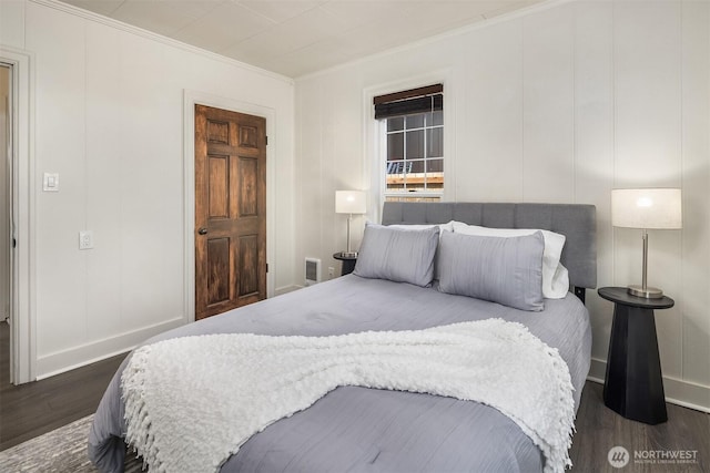 bedroom featuring ornamental molding, baseboards, a decorative wall, and dark wood finished floors
