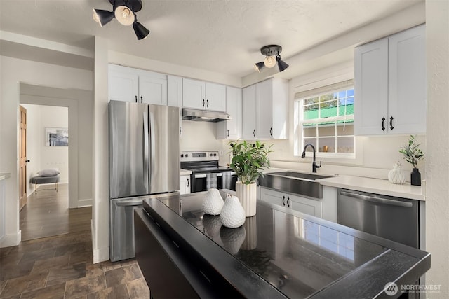 kitchen with stone finish floor, white cabinetry, a sink, appliances with stainless steel finishes, and under cabinet range hood