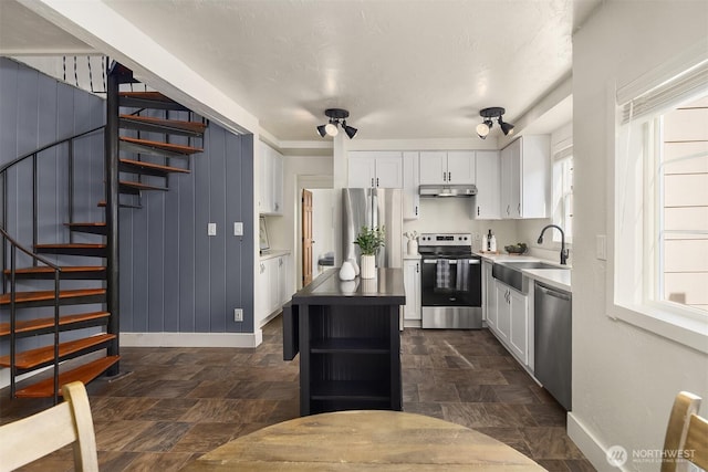 kitchen with a sink, under cabinet range hood, open shelves, white cabinetry, and appliances with stainless steel finishes
