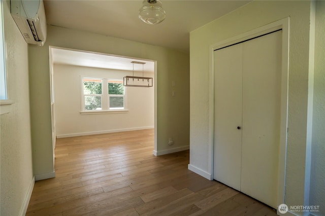 unfurnished bedroom featuring hardwood / wood-style floors, baseboards, a closet, and a wall unit AC
