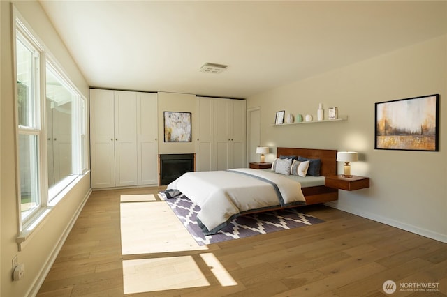 bedroom with baseboards, multiple windows, and light wood-type flooring
