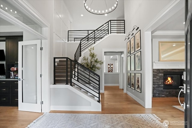 stairway featuring a notable chandelier, wood finished floors, a glass covered fireplace, a high ceiling, and ornamental molding