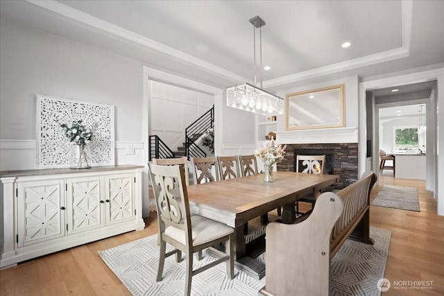 dining area with a wainscoted wall, light wood-style floors, a decorative wall, a fireplace, and stairs