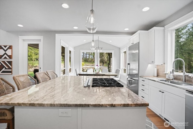 kitchen with white cabinets, a sink, light stone countertops, a center island, and appliances with stainless steel finishes