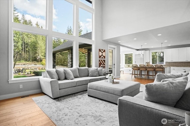 living area featuring recessed lighting, baseboards, a high ceiling, and light wood-type flooring
