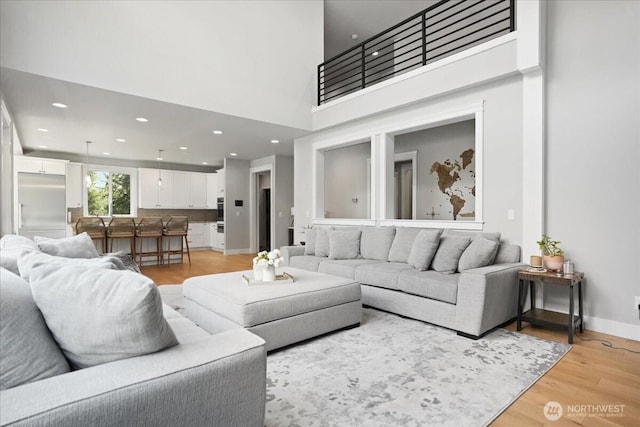 living area featuring recessed lighting, light wood-style flooring, a towering ceiling, and baseboards