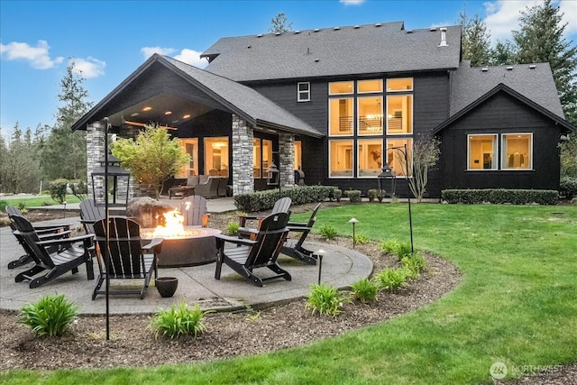 rear view of house with a patio area, an outdoor fire pit, roof with shingles, and a yard