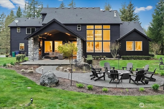 rear view of property with an outdoor living space with a fire pit, stone siding, a shingled roof, a yard, and a patio