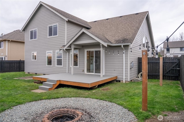 1509 Seahawk Dr, Ferndale, WA 98248 - back of house with a shingled roof, a wooden deck, a fenced backyard, a lawn, and a fire pit