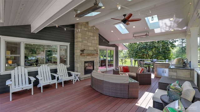 deck featuring an outdoor kitchen, ceiling fan, an outdoor living space with a fireplace, and a sink