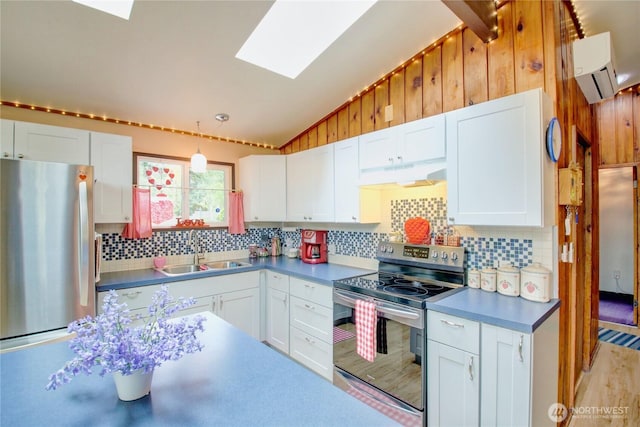 kitchen featuring vaulted ceiling with skylight, tasteful backsplash, a sink, under cabinet range hood, and stainless steel appliances